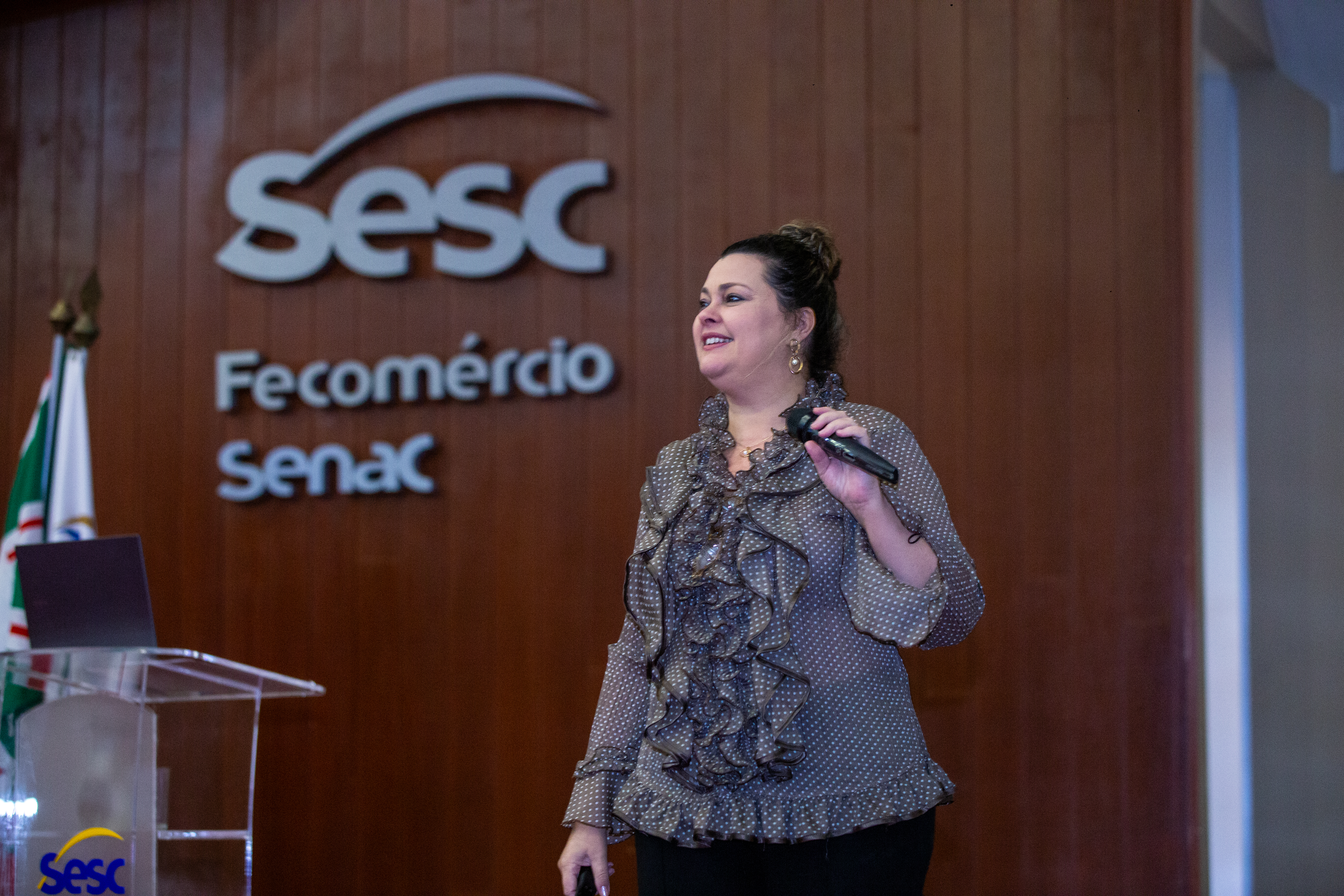 Claudiane Junqueira falando ao microfone em uma palestra